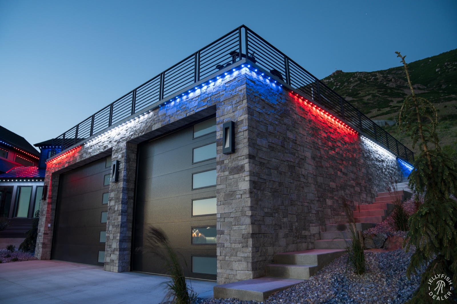 Permanent holiday lighting on a modern home — patriotic red, white, and blue along the rooftop and eaves at twilight