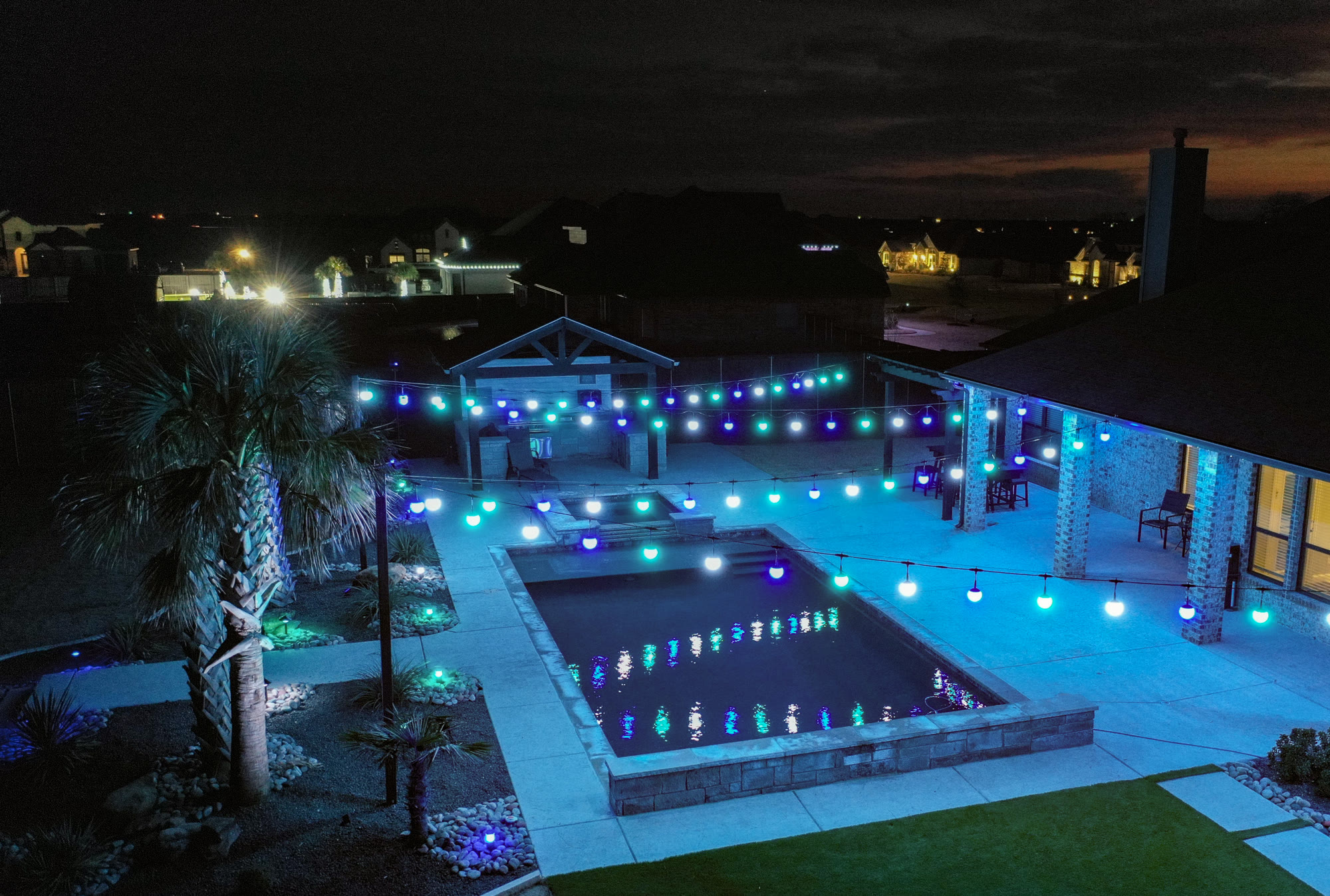 Backyard pool surrounded by permanent patio string lights